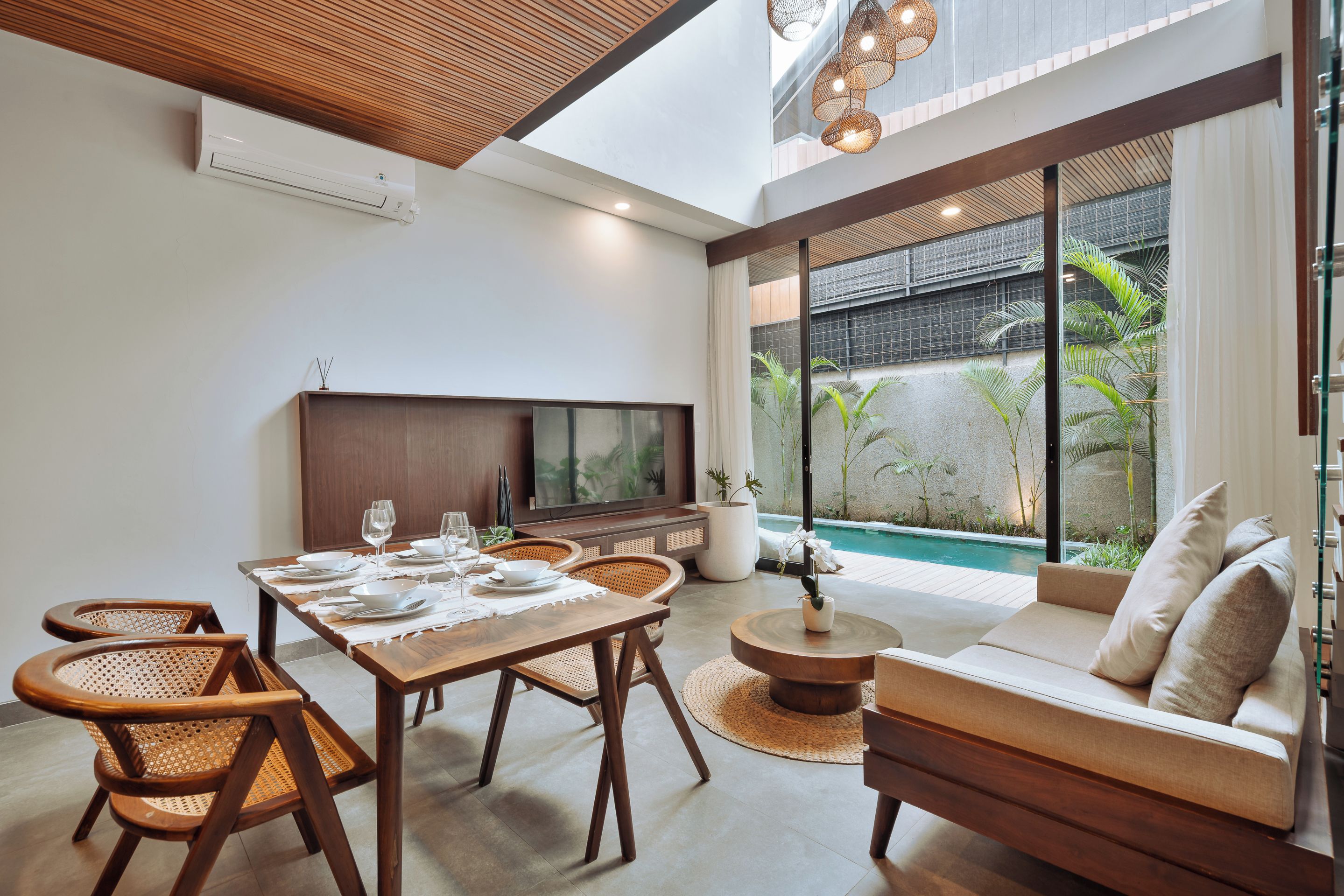 A modern living room with a dining area, a flat-screen TV, and a view of a pool.