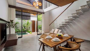 A modern dining area with a wooden table, wicker chairs, and a glass staircase. - Aluna Ubud Villas (Ubud)