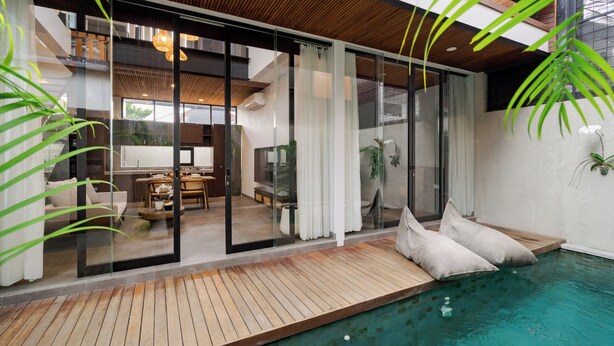 A modern house with a pool, wooden deck, and glass doors leading to a living area with furniture. - Aluna Ubud Villas (Ubud)