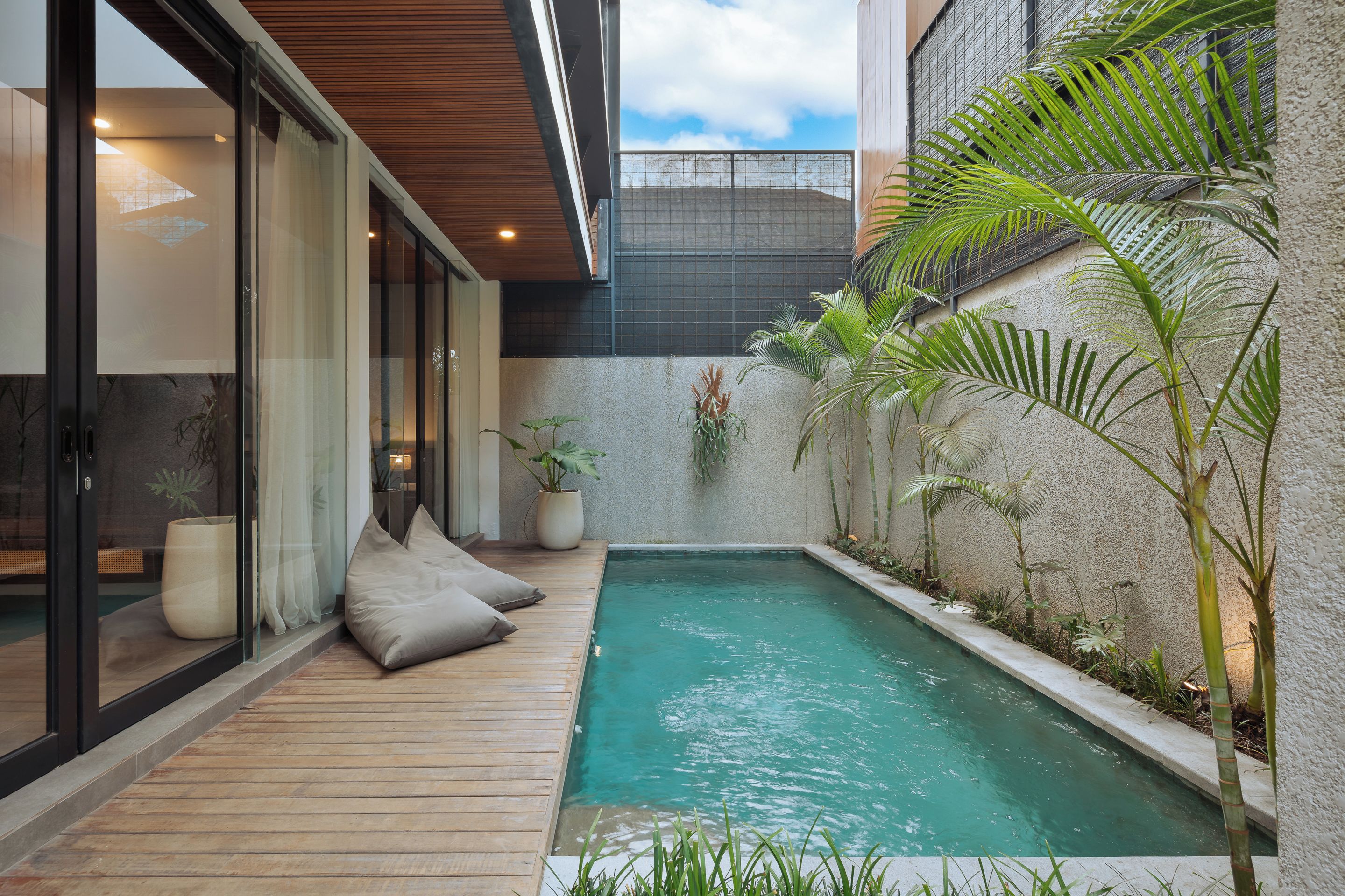 A modern outdoor pool area with a wooden deck, glass doors, and potted plants.