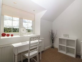 Habitación con escritorio blanco, silla, radiador, ventana con vista y estante con un letrero.