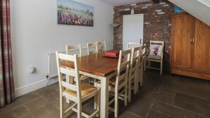 Een eetgedeelte met een houten tafel en stoelen, een schilderij aan de muur, een bakstenen muur en een trap.