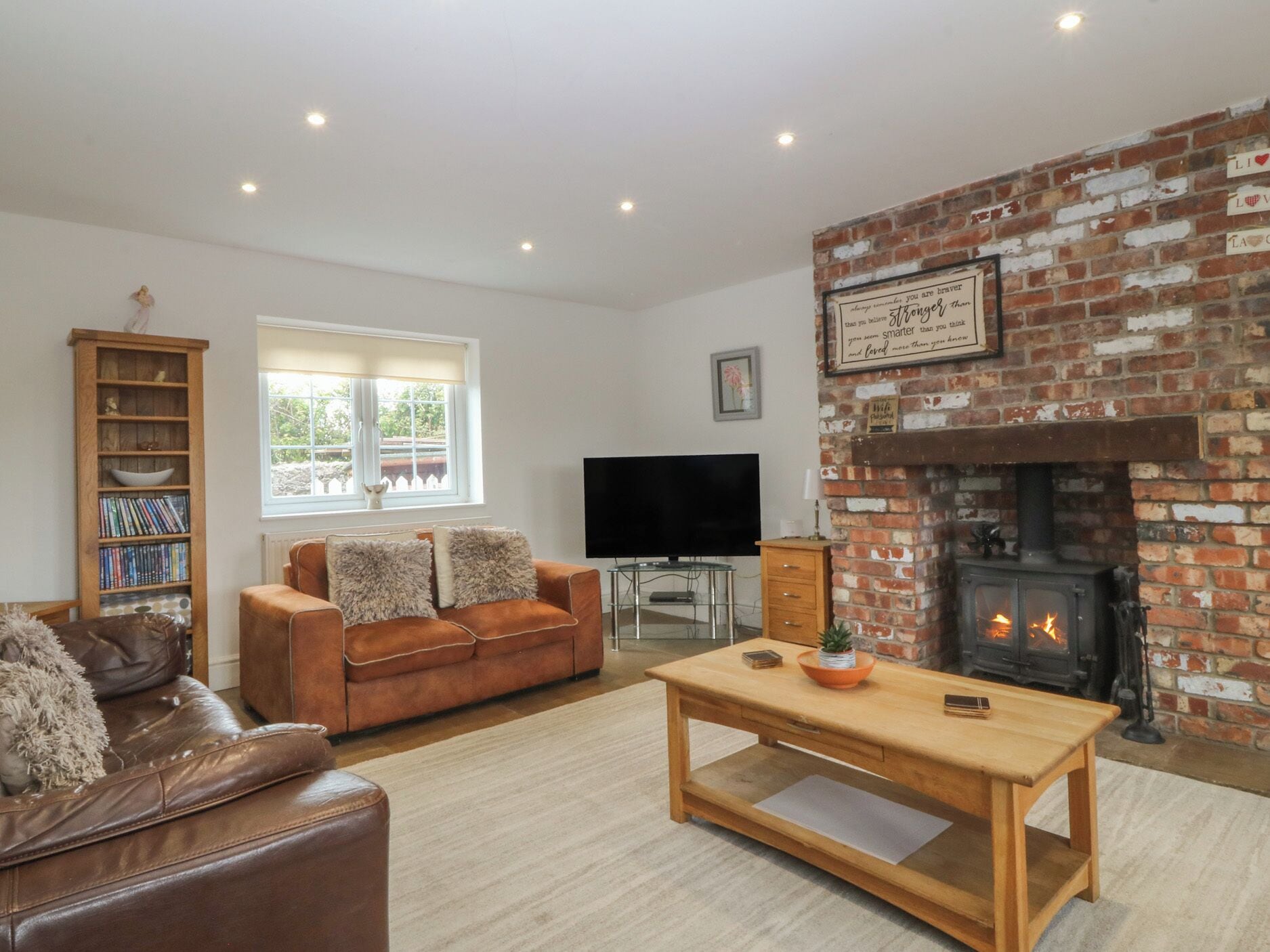 A living room with a brick fireplace, a leather sofa, a wooden coffee table, a bookshelf, and a television.