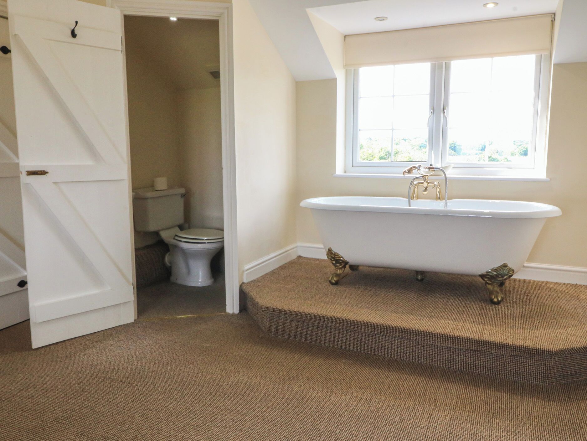 A bathroom with a freestanding bathtub, a toilet, and a window.