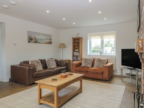 A living room with two brown leather sofas, a wooden coffee table, a bookshelf, a TV, and a painting on the wall. - Llanallgo Church Rooms (Moelfre)