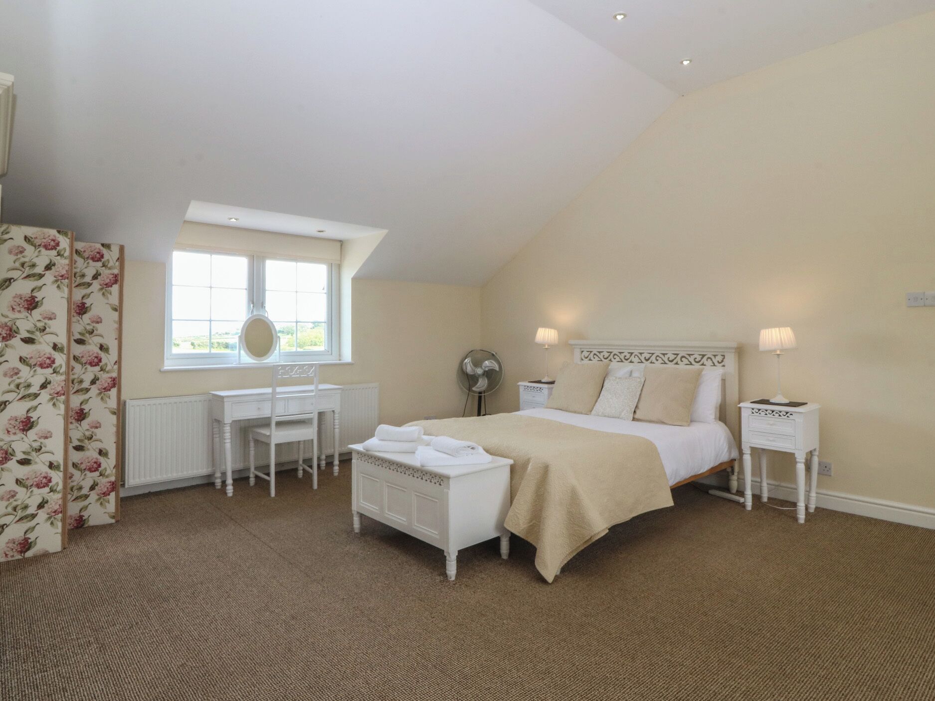 A bedroom with a bed, bedside tables, a desk, a chair, a radiator, and a window.