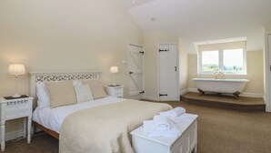 Een slaapkamer met een bed, nachtkastjes, een dressoir, een badkuip en een raam met uitzicht.