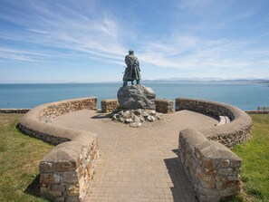 A circular stone structure with a statue in the center, surrounded by a paved walkway. - Llanallgo Church Rooms (Moelfre)