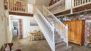 Een trap met witte balustrades die leidt naar een hoger gelegen deel, een eettafel met stoelen en een houten kast.