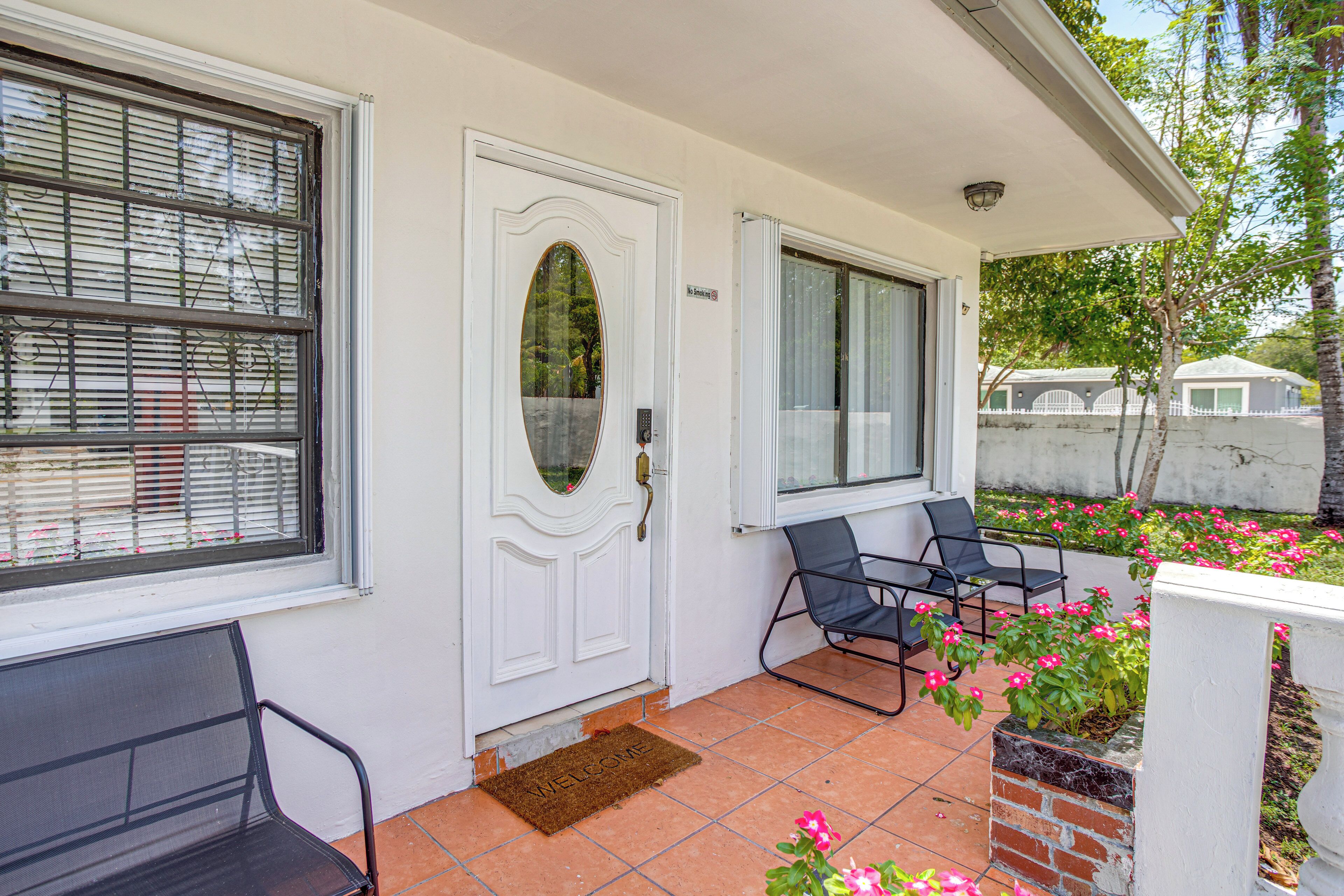 Una casa con una puerta blanca, una ventana con persianas, un banco y una silla afuera.