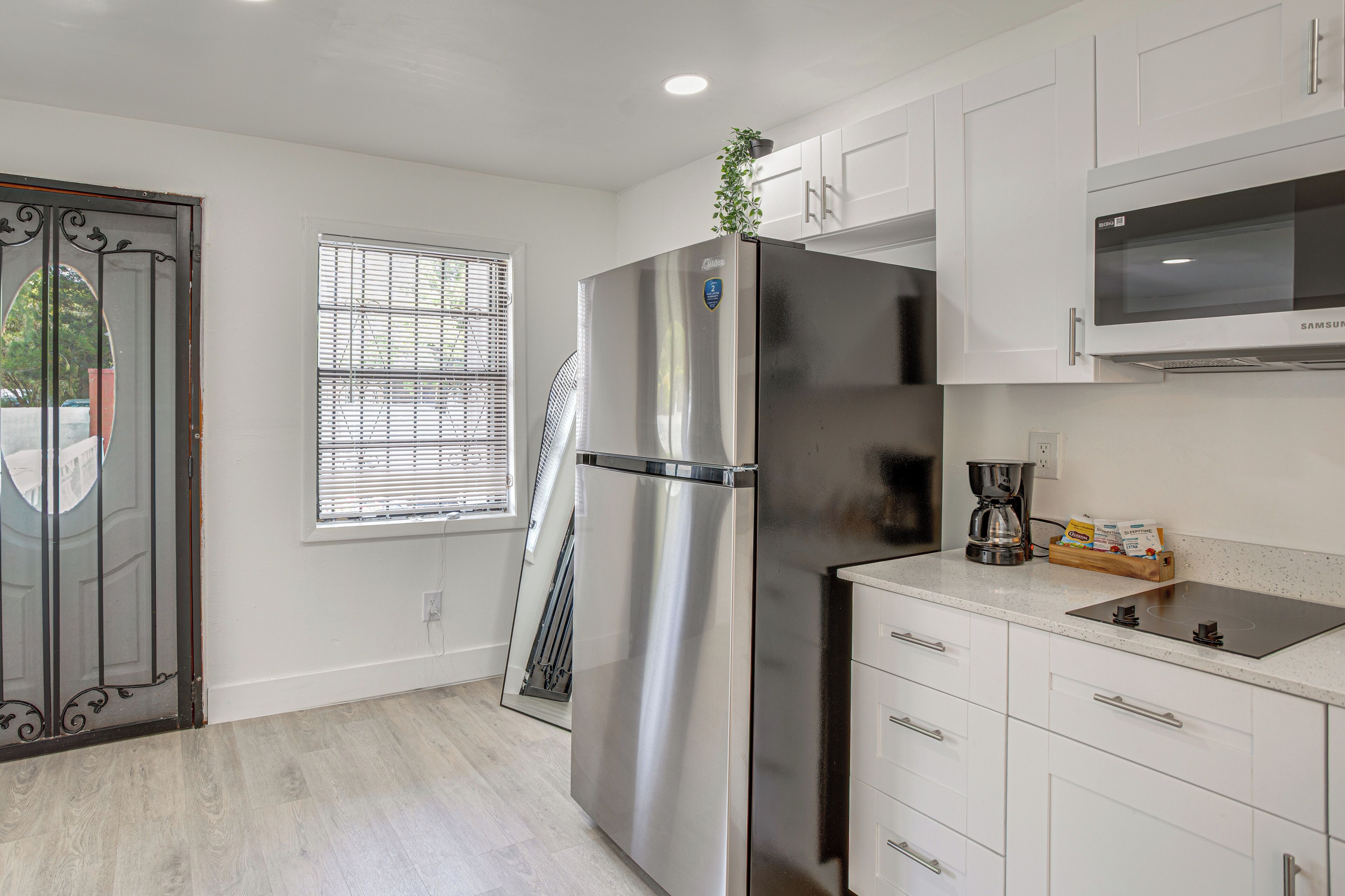 Una cocina moderna con electrodomésticos de acero inoxidable, armarios blancos, un microondas y una ventana con persianas.