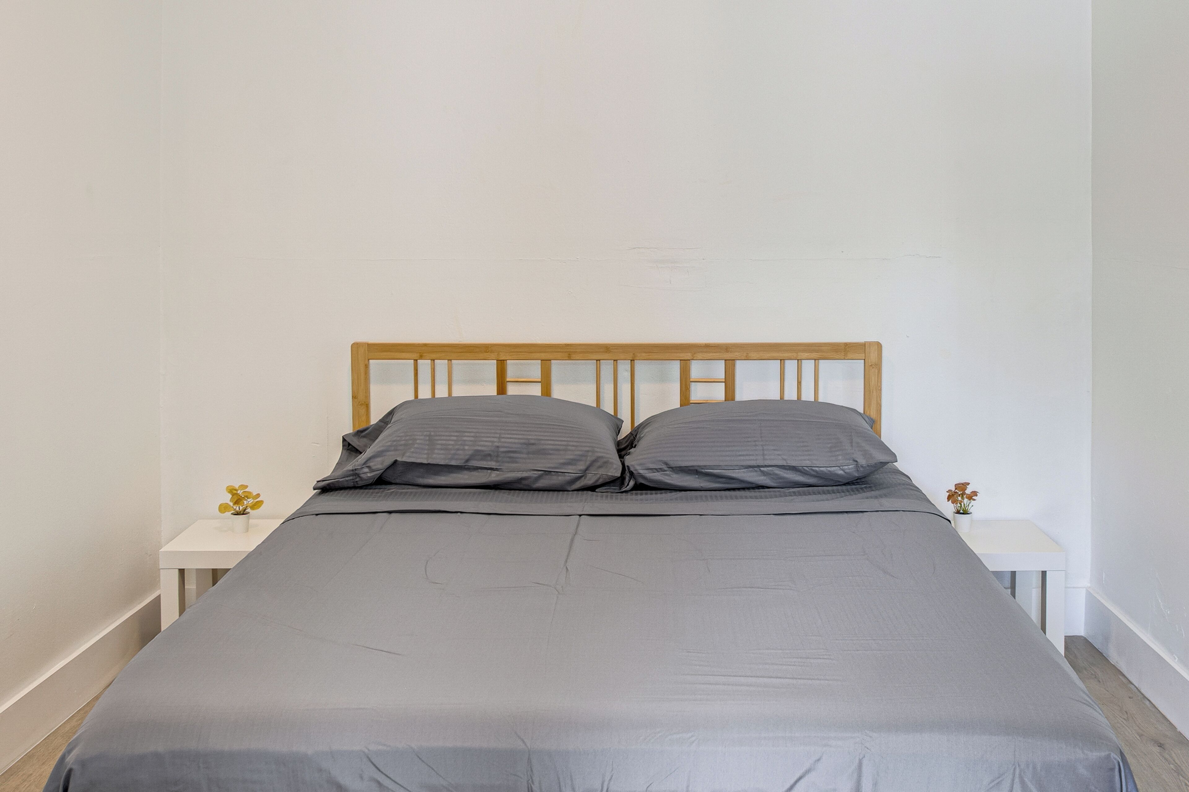 Un lit simple avec une tête de lit en bois, une literie grise et deux tables de chevet ornées de petits vases.