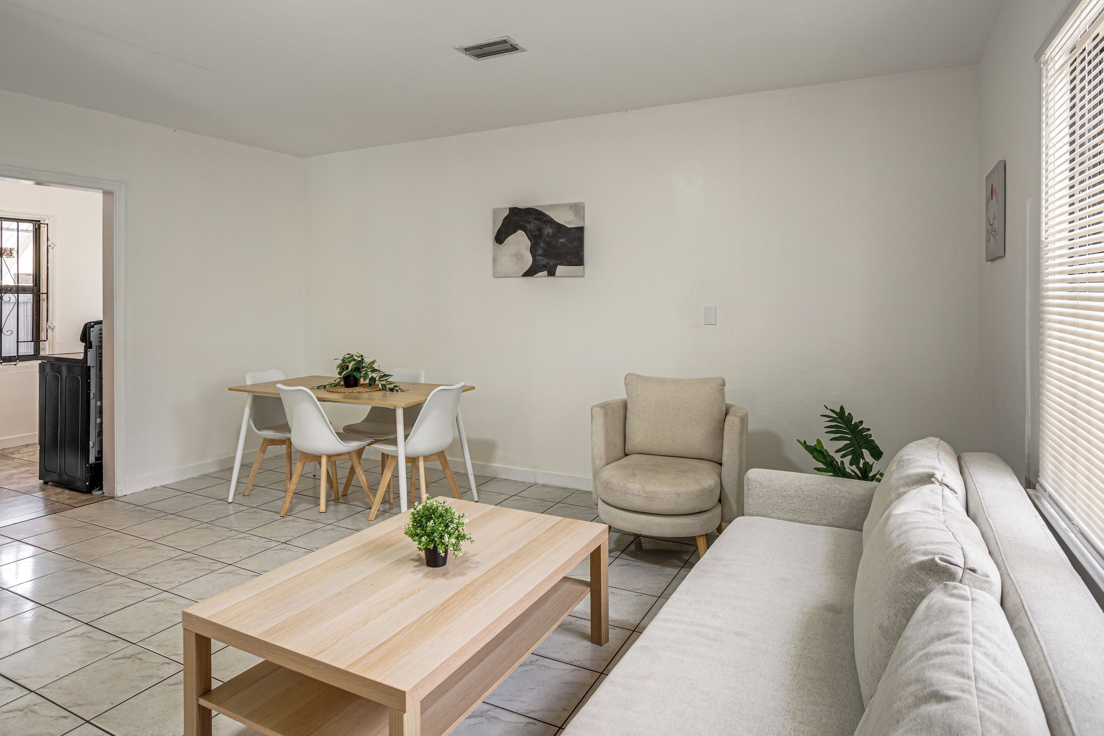 A modern living room with a sofa, a coffee table, a dining table with chairs, and a painting on the wall.