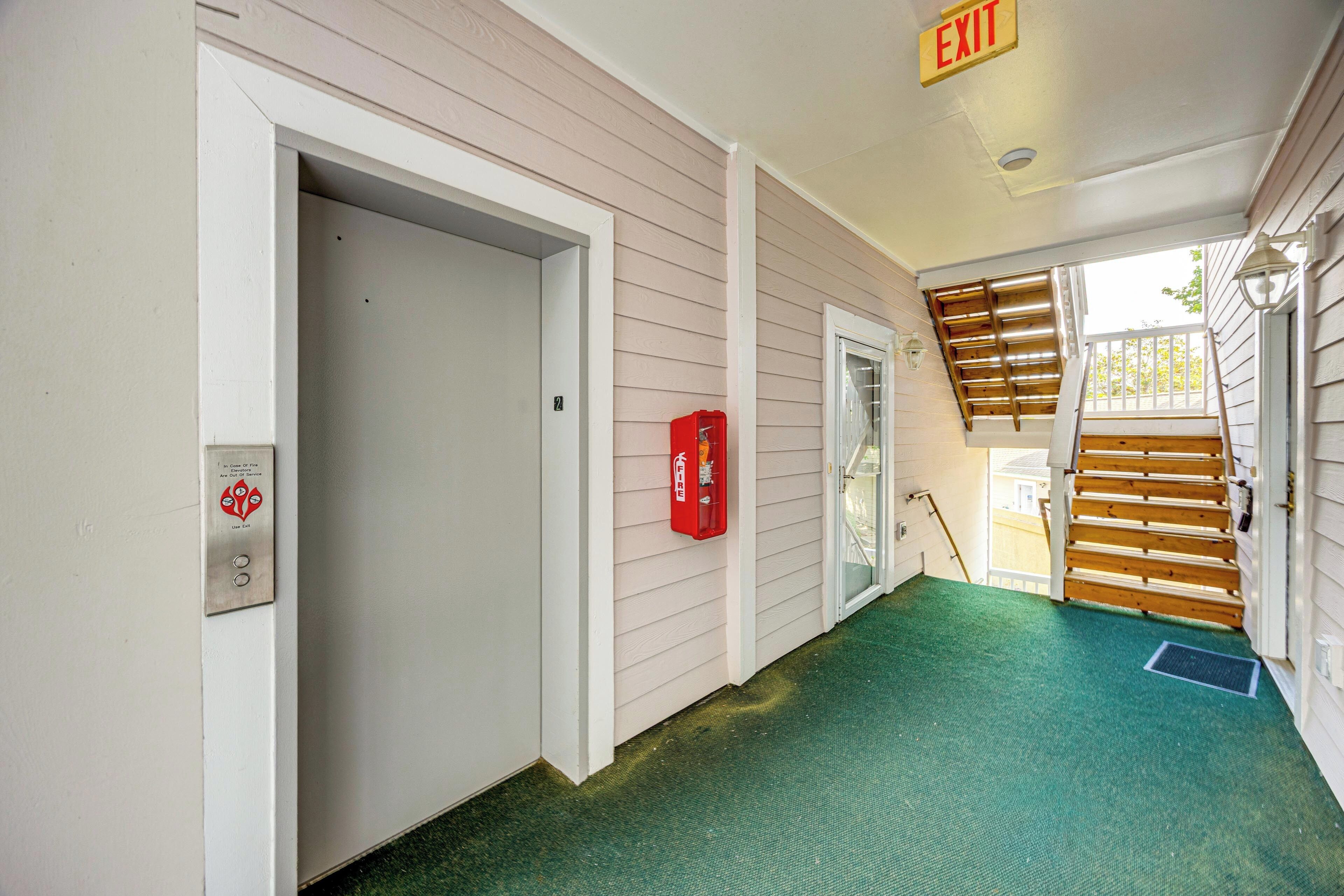 A hallway with a green carpet, a fire alarm, an exit sign, and a staircase.