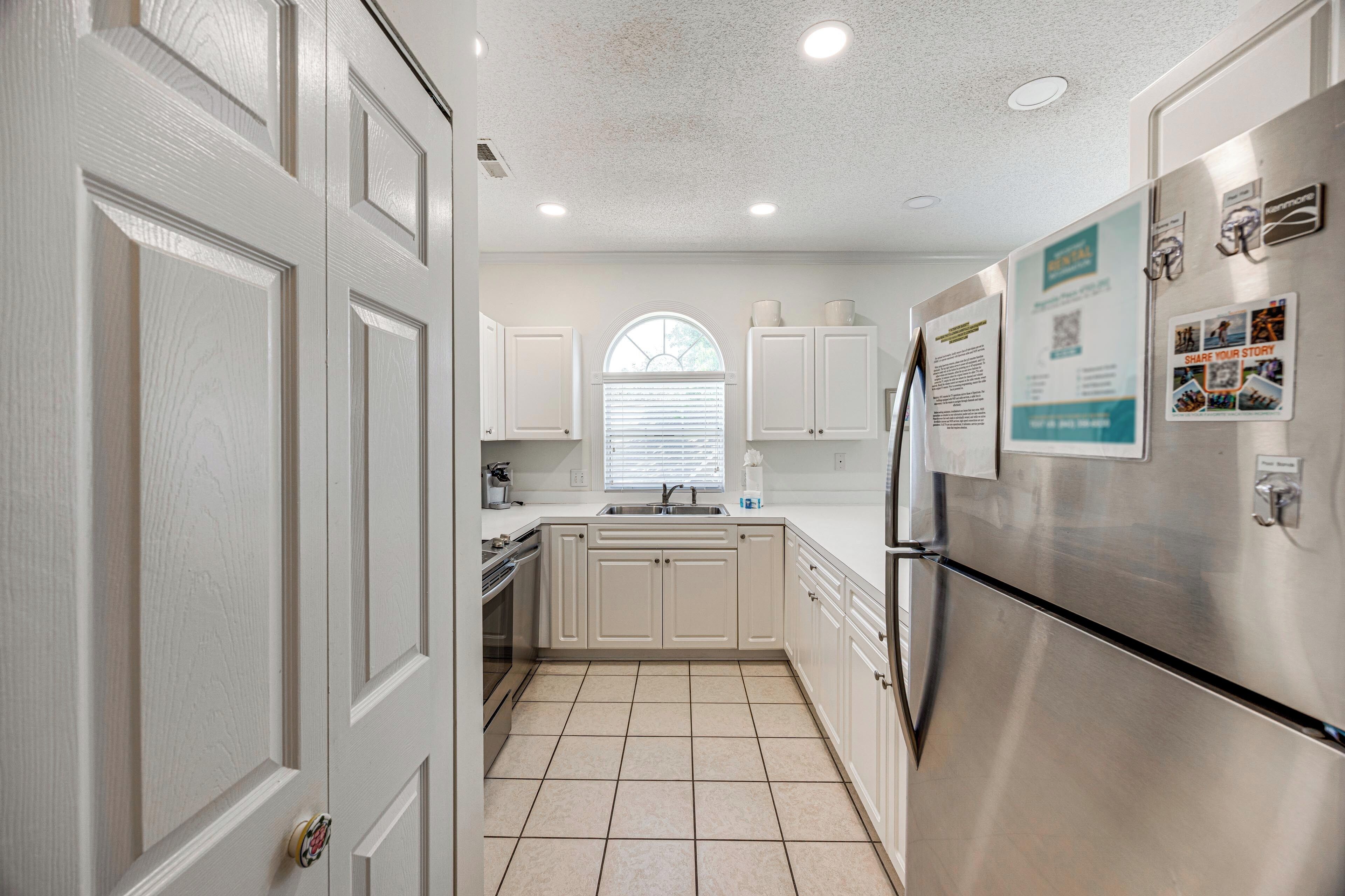 A kitchen with white cabinetry, a stainless steel refrigerator, and a window with blinds.