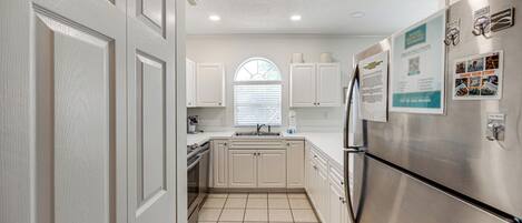 A kitchen with white cabinetry, a stainless steel refrigerator, and a window with blinds.