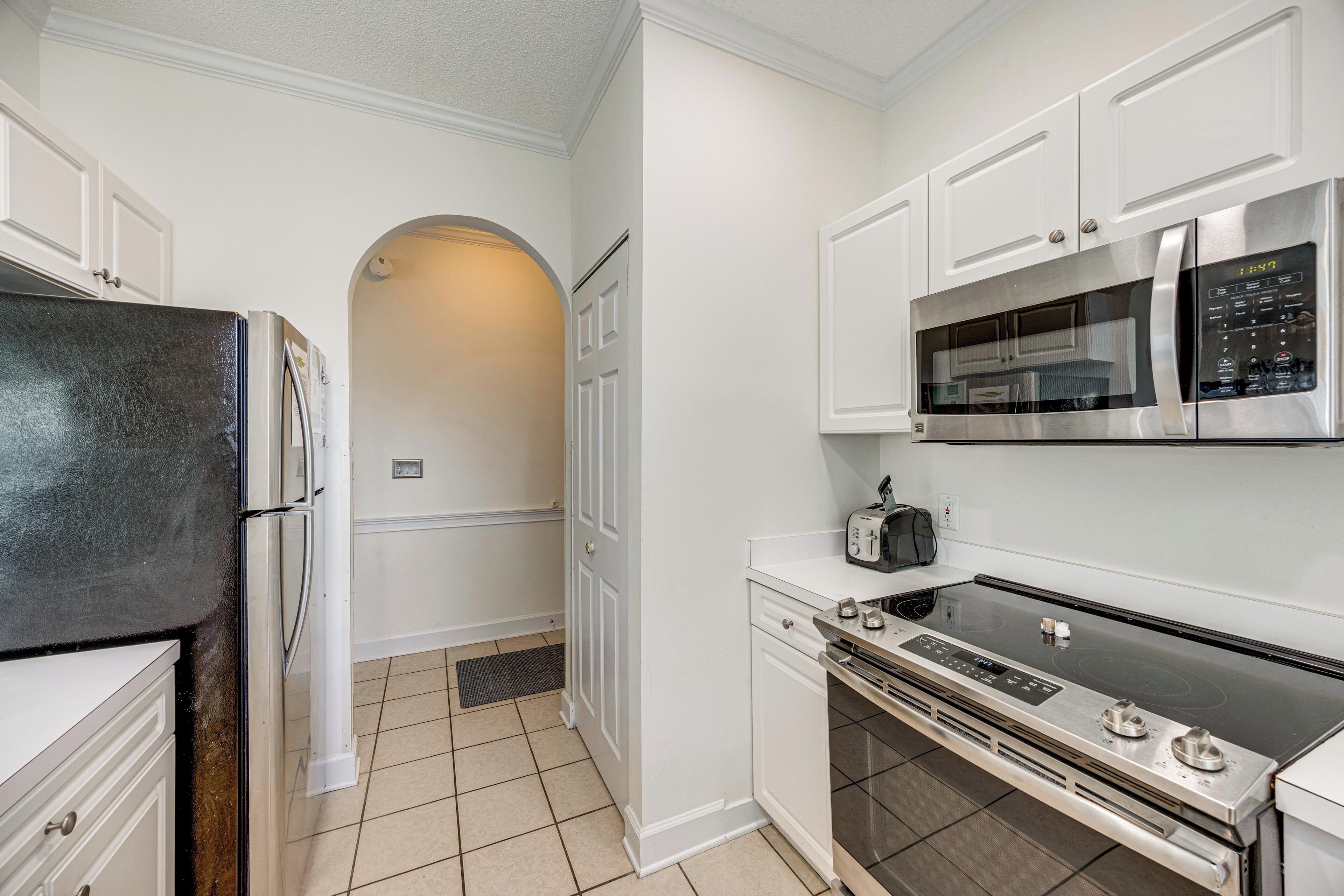 A kitchen with white cabinetry, a stainless steel refrigerator, a microwave, a stove, and a toaster.