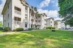 A multi-story residential building with balconies, a well-maintained lawn, and parked cars. - Tee Times & Poolside Vibes! Myrtle Beach Retreat (Myrtle Beach)