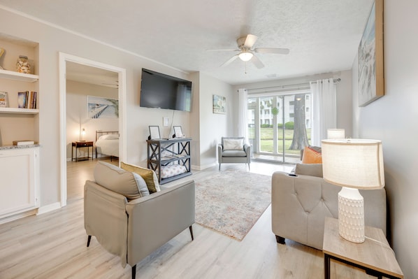 A living room with a sofa, armchair, TV, and a lamp on a side table. - Tee Times & Poolside Vibes! Myrtle Beach Retreat (Myrtle Beach)