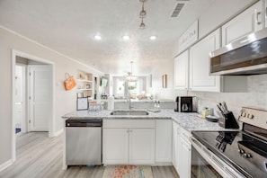 A modern kitchen with white cabinetry, a built-in dishwasher, a stainless steel stove, and a coffee bar sign. - Tee Times & Poolside Vibes! Myrtle Beach Retreat (Myrtle Beach)