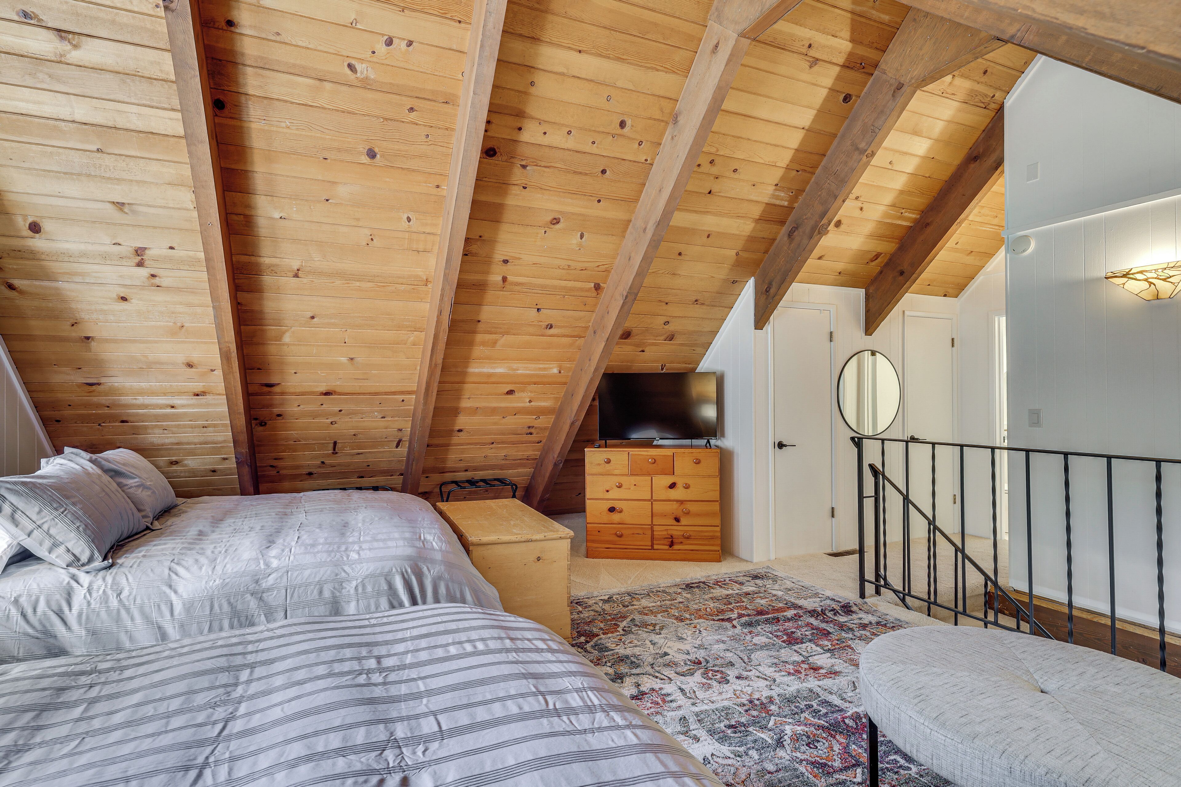 A bedroom with a sloped ceiling, wooden beams, a bed with striped bedding, a dresser, and a rug.