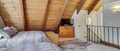 A bedroom with a sloped ceiling, wooden beams, a bed with striped bedding, a dresser, and a rug.