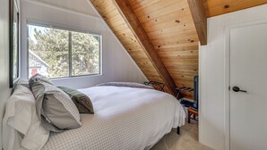 Una camera da letto con soffitto spiovente, un letto con cuscini, una finestra e una porta.