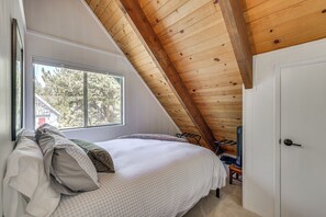 Ein Schlafzimmer mit schrägem Dach, einem Bett mit Kissen, einem Fenster und einer Tür.