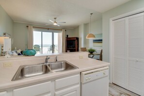 A kitchen with a double sink, white cabinets, a ceiling fan, and a view of the outdoors. - Walk to Beach! The Dunes Condo w/ Resort Perks (Gulf Shores)