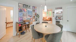 A modern dining area with a round table, grey chairs, and a wall adorned with framed pictures. - Tremont Retreat w/ Putting Green Near Downtown (Cleveland)
