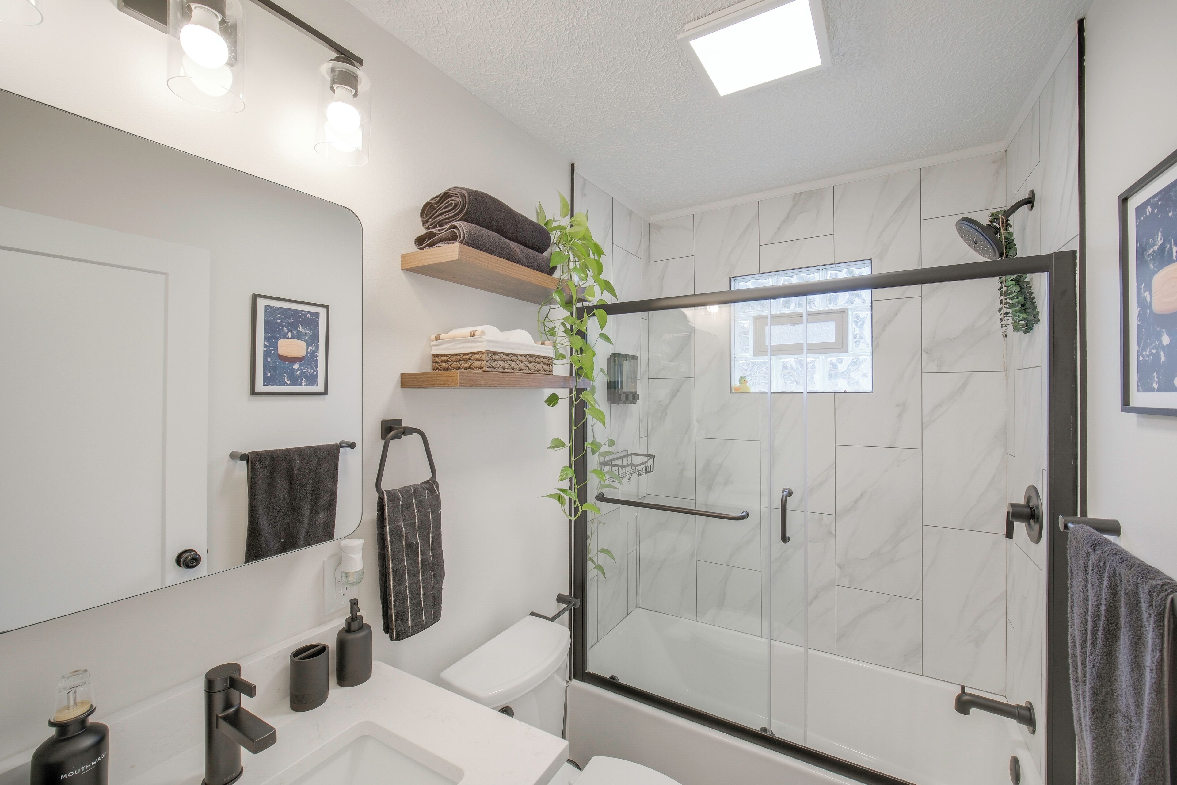 Un baño moderno con ducha de vidrio, un lavamanos blanco y un espejo encima.