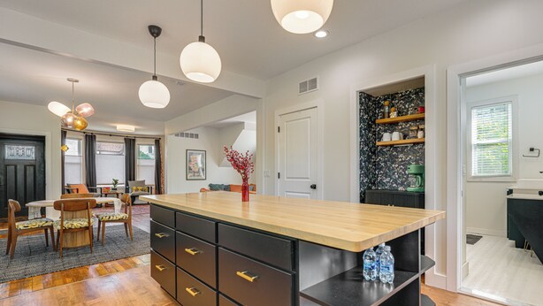 A modern kitchen with a wooden island, black cabinets, and pendant lighting. - Yard & Fire Pit! Chic Retreat, 2 Mi to Ford Field (Detroit)