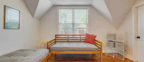 Une chambre située dans un espace de type « loft », avec un plafond en pente, un lit doté d’une tête de lit, une fenêtre avec des stores, une porte et un meuble de rangement.