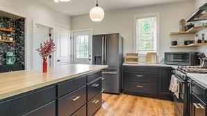 A modern kitchen with a central island, black cabinetry, stainless steel appliances, and a wooden floor. - Yard & Fire Pit! Chic Retreat, 2 Mi to Ford Field (Detroit)