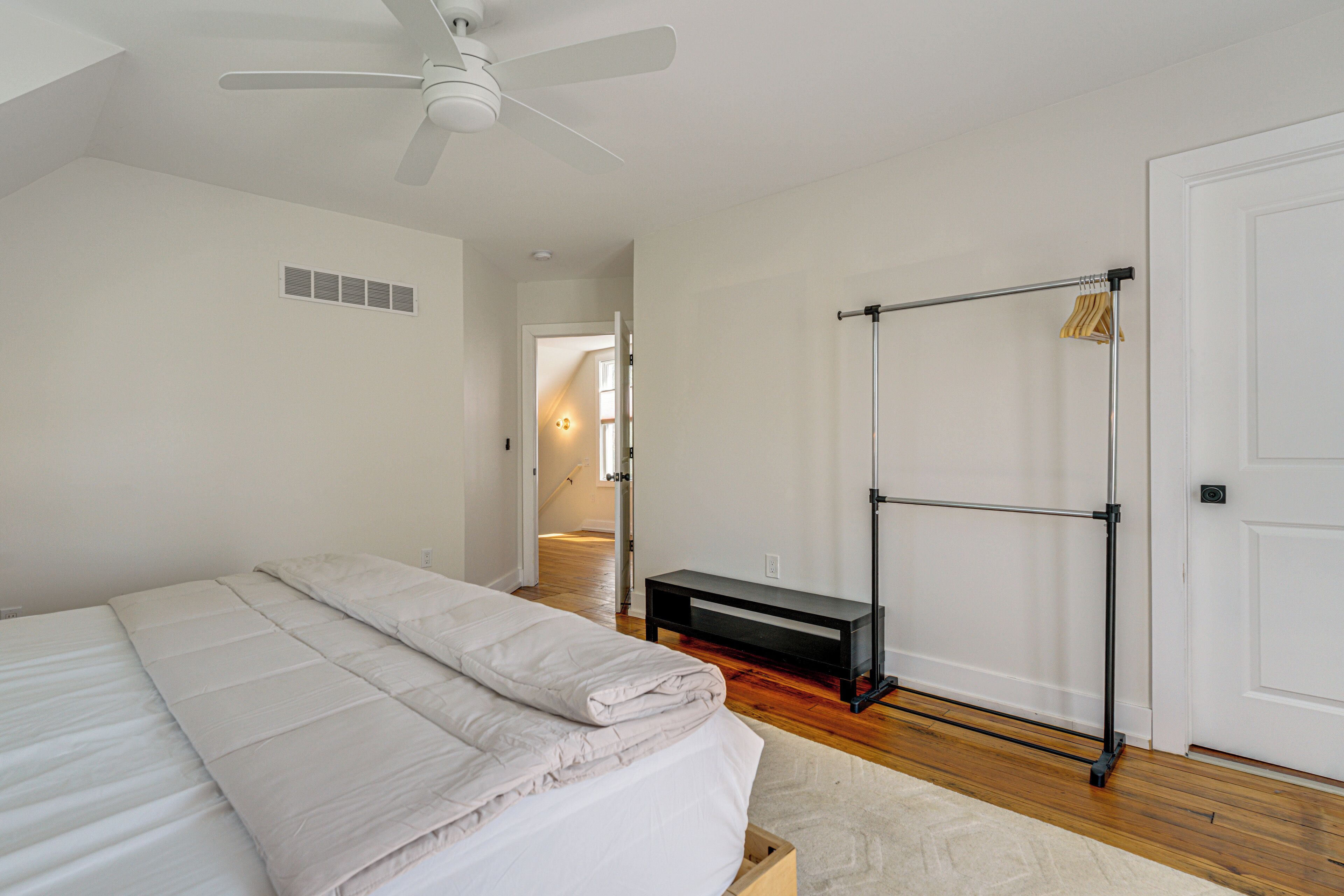 A bedroom with a bed, a ceiling fan, a bench, and a clothing rack.