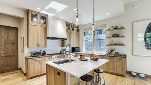 A modern kitchen with wooden cabinets, a central island with stools, a microwave, and a sink. - Walk to Town & Trails! Luxe Mtn Retreat w/ Hot Tub (Ketchum)