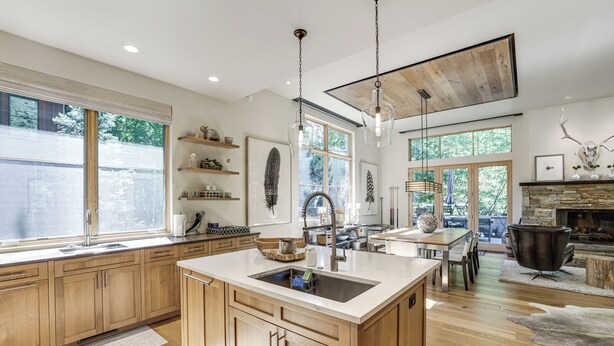 A modern kitchen with wooden cabinets, a large island with a sink, pendant lighting, and a stone fireplace. - Walk to Town & Trails! Luxe Mtn Retreat w/ Hot Tub (Ketchum)