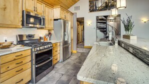 Cozinha com armários de madeira, eletrodomésticos de aço inoxidável e bancada de granito.