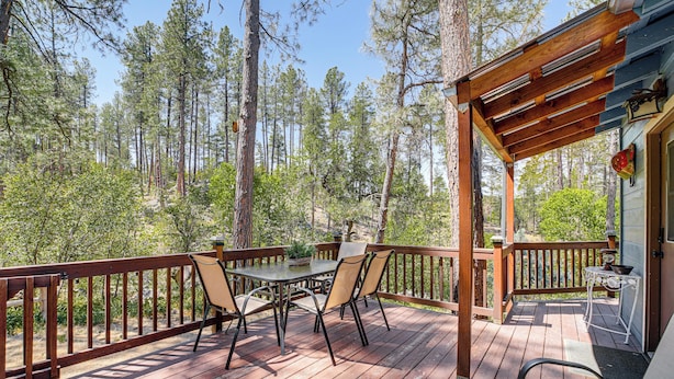 A wooden deck with a table and chairs, surrounded by tall trees. - Deck, Trails & Forest Views! Ponderosa Park Cabin (Prescott)