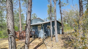 A rustic cabin surrounded by tall trees, with a wooden deck and a stone wall. - Deck, Trails & Forest Views! Ponderosa Park Cabin (Prescott)