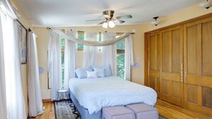 Ein Schlafzimmer mit einem Bett, einem Deckenventilator, einem Holzschrank und einem kleinen Tisch.