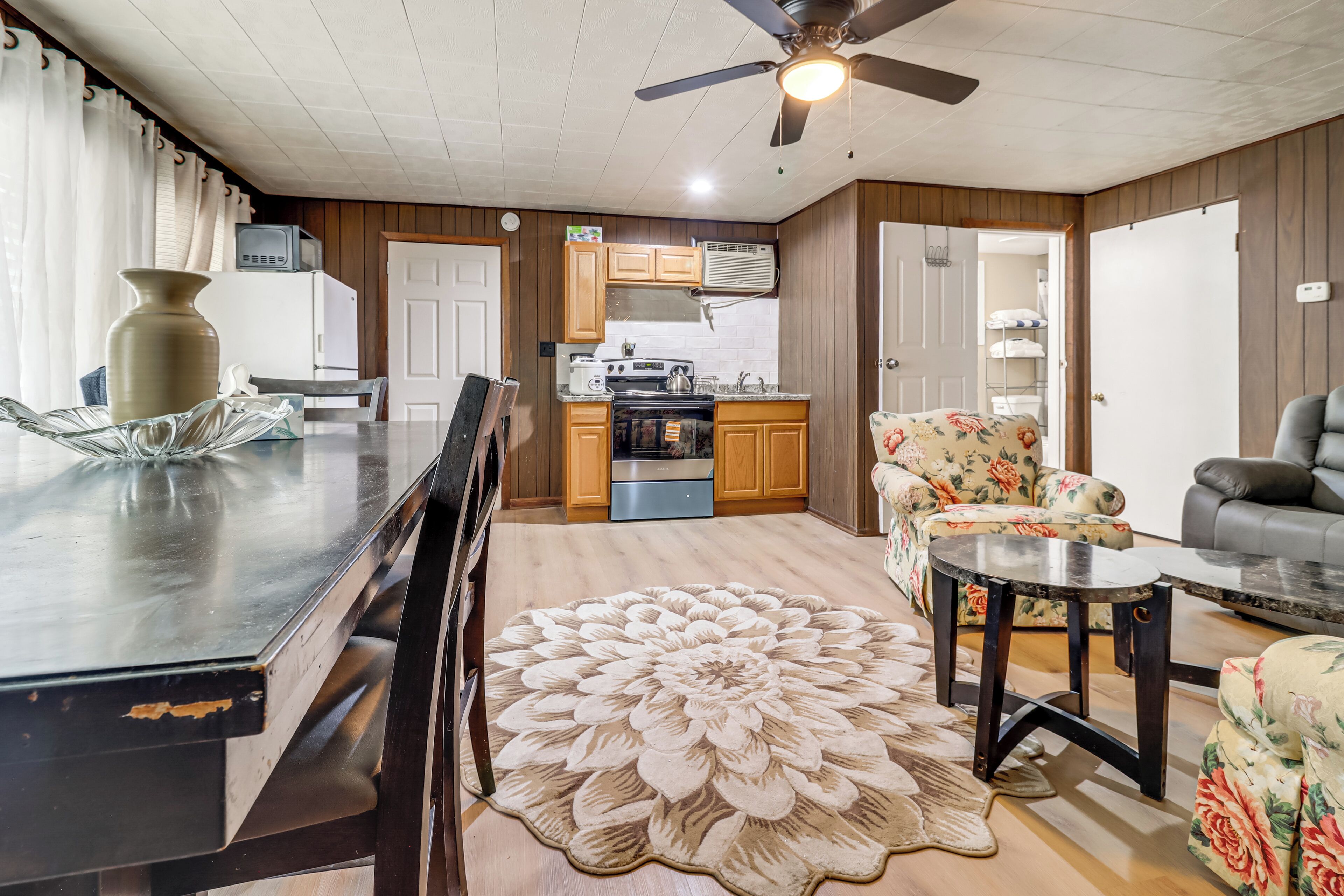 A kitchen with a refrigerator, stove, and microwave. There is a dining table with chairs and a decorative rug.