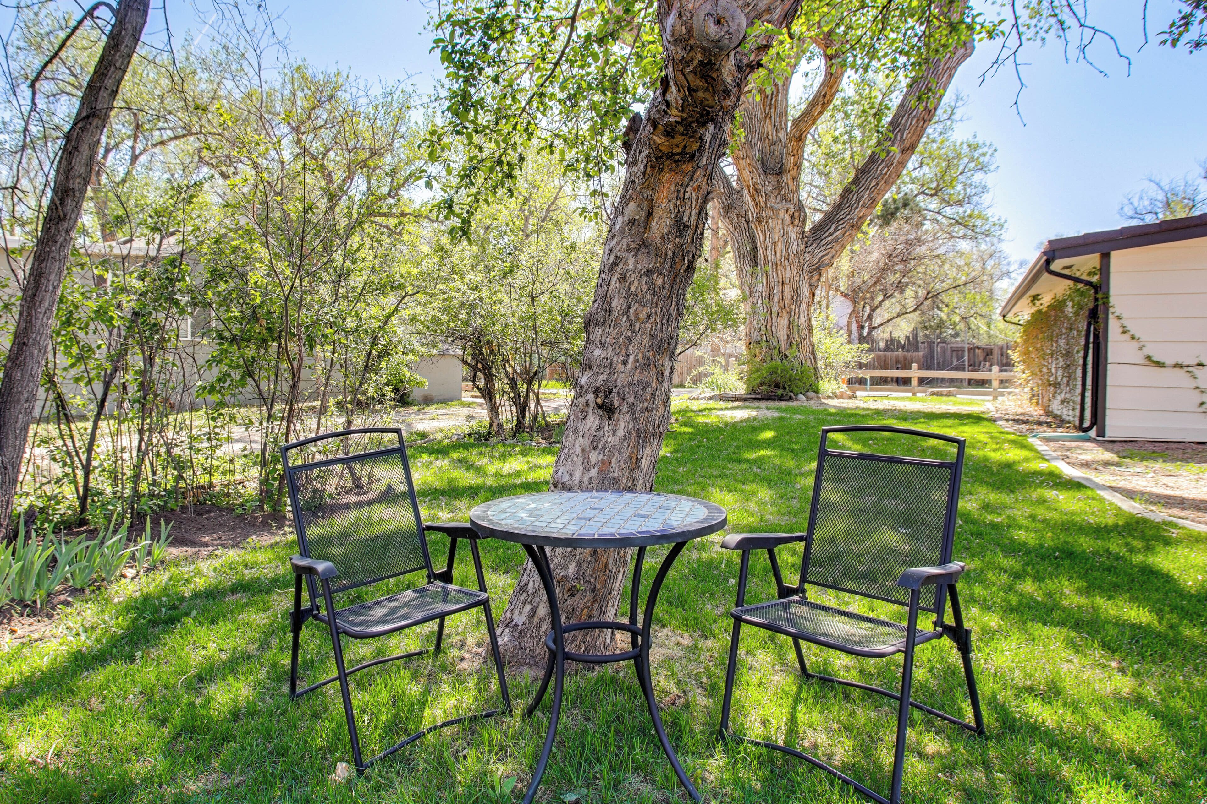 A patio with a round table and two chairs, surrounded by trees and a building.