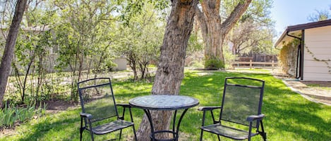 Une terrasse avec une table ronde et deux chaises, entourée d’arbres et d’un bâtiment.