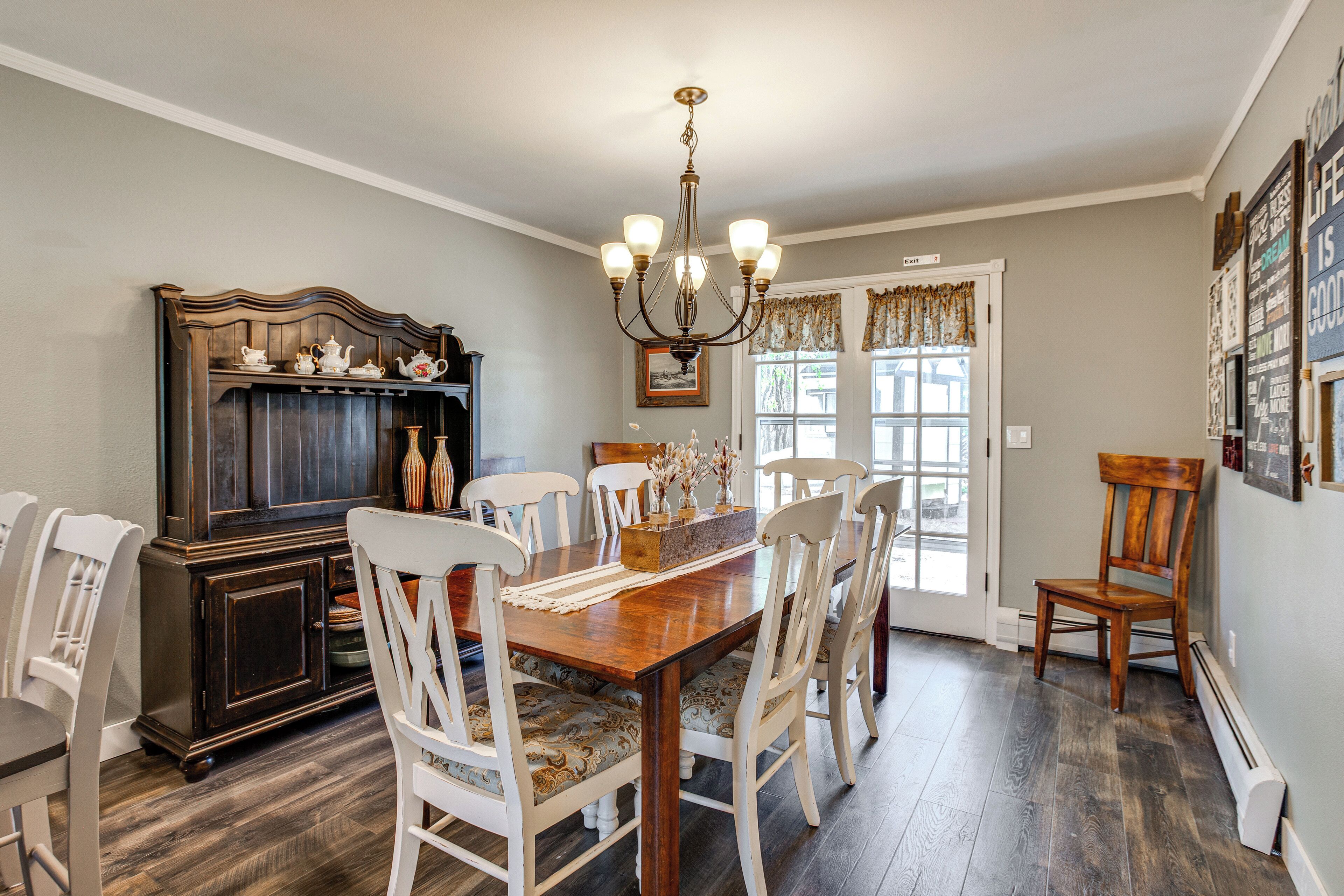 A dining room with a wooden table, white chairs, a chandelier, and a dark wooden cabinet.
