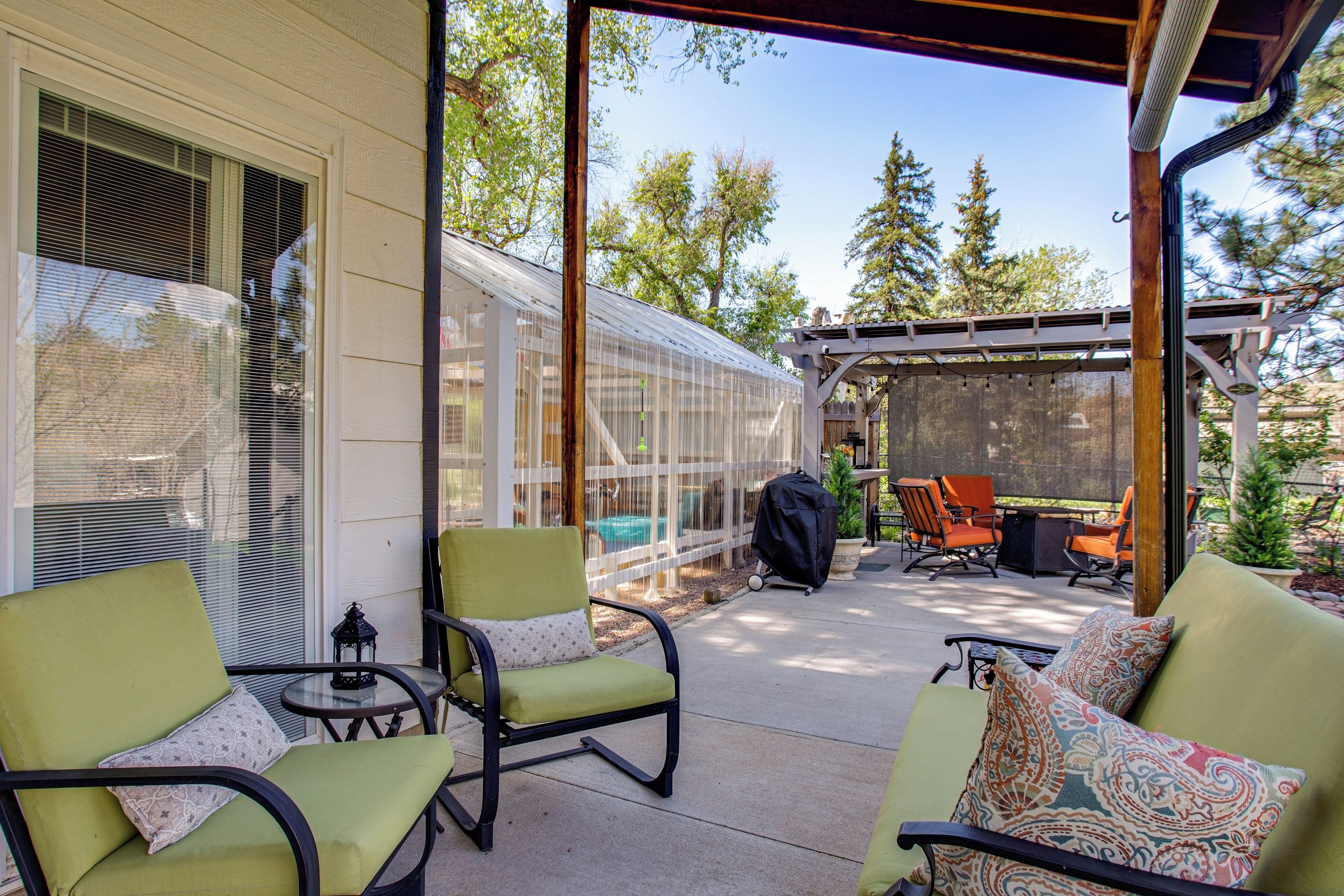 A covered patio with outdoor furniture, a greenhouse, and a barbecue grill.