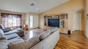 A living room with a large sectional sofa, a flat-screen TV, wooden flooring, and built-in shelving. - Patio & Grill! Resort-style Sun Lakes Escape (Chandler)