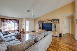 A living room with a large sectional sofa, a flat-screen TV, wooden flooring, and built-in shelving. - Patio & Grill! Resort-style Sun Lakes Escape (Chandler)
