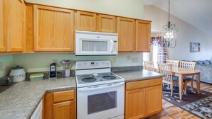 A kitchen with wooden cabinets, a white microwave, a stove, and a dining area with a table and chairs. - Patio & Grill! Resort-style Sun Lakes Escape (Chandler)