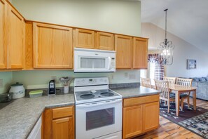 A kitchen with wooden cabinets, a white microwave, a stove, and a dining area with a table and chairs. - Patio & Grill! Resort-style Sun Lakes Escape (Chandler)